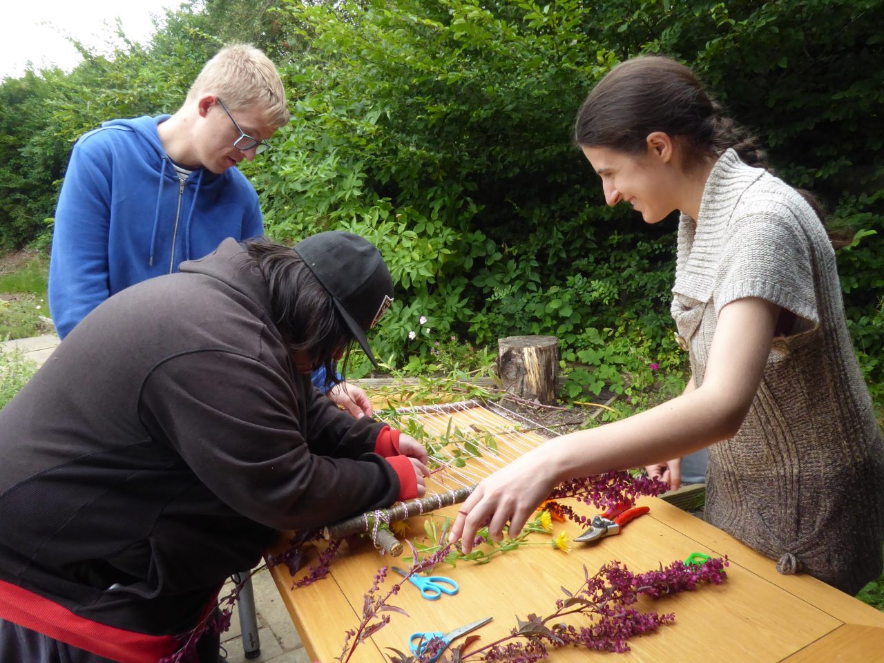 A photo of a group weaving together flowers and foliage to make an art installation.